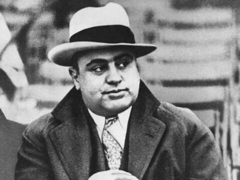 Al Capone: Ascensão e Queda do Rei do Crime na Lei Seca Retrato de Al Capone, um dos mais notórios gângsteres da era da Lei Seca. Capone enriqueceu com o contrabando e a venda ilegal de álcool, tornando-se o símbolo da criminalidade organizada que floresceu durante a proibição e desafiou as autoridades. Na imagem, Al Capone, é flagrado enquanto assistia a um jogo de futebol americano. Esta imagem captura um momento de lazer do notório gângster, contrastando com sua vida de crimes.