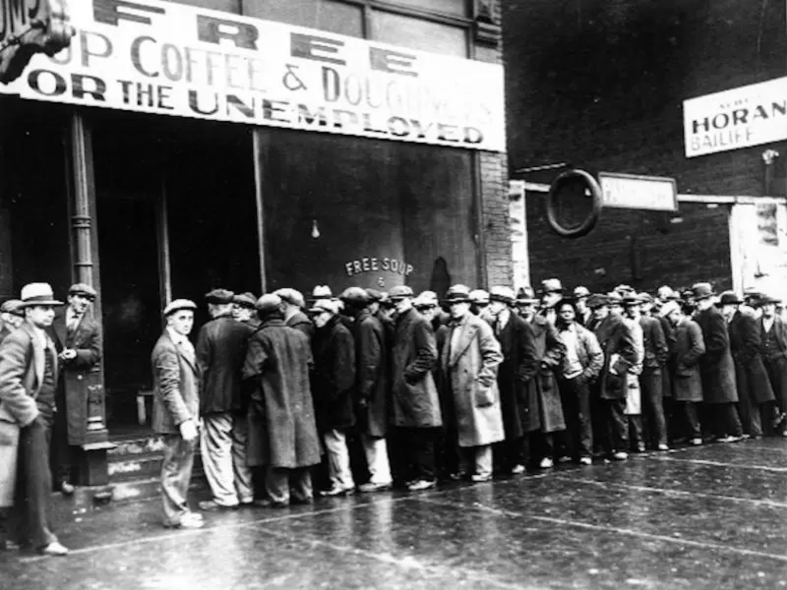 Trabalhadores desempregados fazem fila para se alimentar de graça em Chicago durante a Grande Depressão. O cartaz anunciava “Copos de café e rosquinhas grátis para os desempregados”. Al Capone foi o primeiro a abrir refeitórios para os trabalhadores desempregados, mostrando seu lado filantrópico.