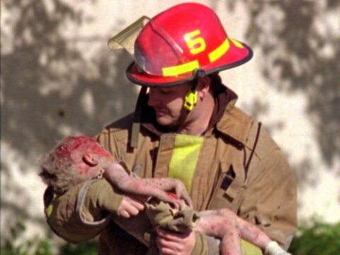 Atentado de Oklahoma City: Terrorismo Doméstico Que Mudou os EUA O bombeiro Chris Fields carrega o corpo sem vida de Baylee Almon, de apenas um ano, uma das 19 crianças mortas na creche America's Kids, após o Atentado de Oklahoma City. Esta fotografia icônica, que ganhou o Prêmio Pulitzer, tornou-se o símbolo mais poderoso da inocência perdida no atentado e do custo humano do extremismo político. Fonte: The Daily Oklahoman Autoria: Charles H. Porter IV (Prêmio Pulitzer 1996).
