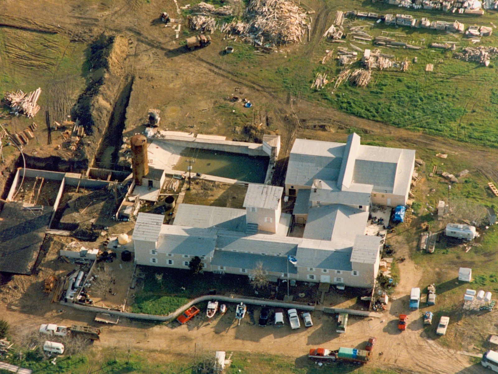 O complexo Monte Carmelo dos Branch Davidians antes do cerco, mostrando a comunidade religiosa em seu estado original. Este conjunto de edifícios abrigava cerca de 130 pessoas, incluindo famílias inteiras que haviam dedicado suas vidas à comunidade liderada por David Koresh. A estrutura principal era um edifício de madeira de vários andares que servia como residência, local de culto e centro comunitário.