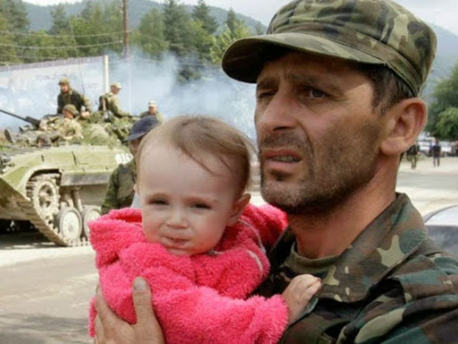 Garotinha é evacuada da área de conflito durante a Guerra dos Cinco Dias. A imagem mostra um soldado georgiano segurando um bebê vestido de rosa, com veículos blindados de transporte de tropas (BMP) do exército georgiano visíveis ao fundo. Foto: David Mdzinarishvili/Reuters.