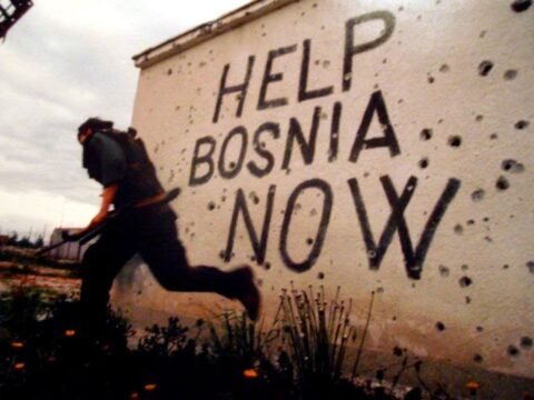 Guerra da Bósnia: Genocídio Esquecido no Coração da Europa Muro crivado de perfurações de armas de fogo com a inscrição em inglês Help Bosnia Now (Ajude a Bósnia Agora). Autor desconhecido.