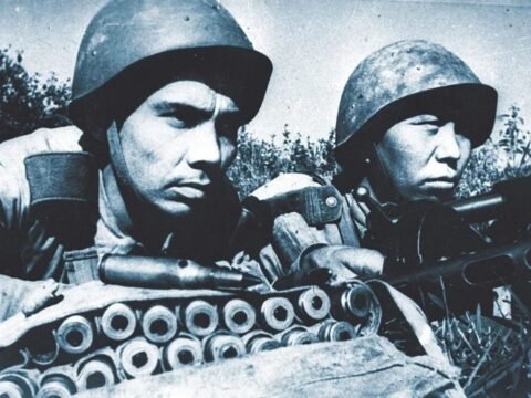 Dois soldados do Exército Vermelho de origem centro-asiática (provavelmente cazaques ou uzbeques) em posição de combate. Os soldados usam capacetes soviéticos padrão e estão equipados com rifles e cinturões de munição.